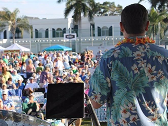Announcer at a Belleair concert wearing a Hawaiian shirt in front of a crowd of attendees.