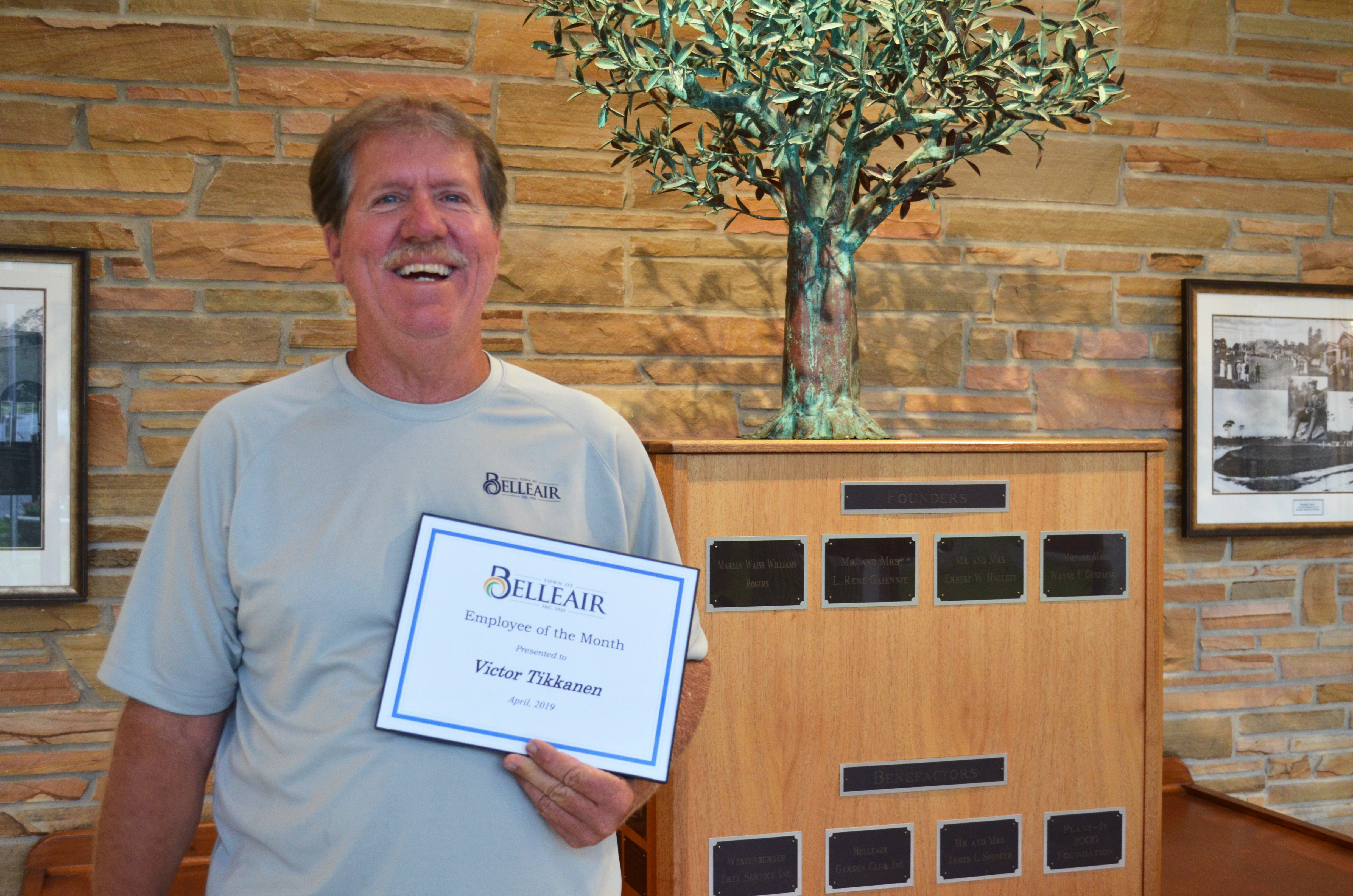 Vic, April's Employee of the Month smiles proudly in the Town Hall lobby holding a certificate 