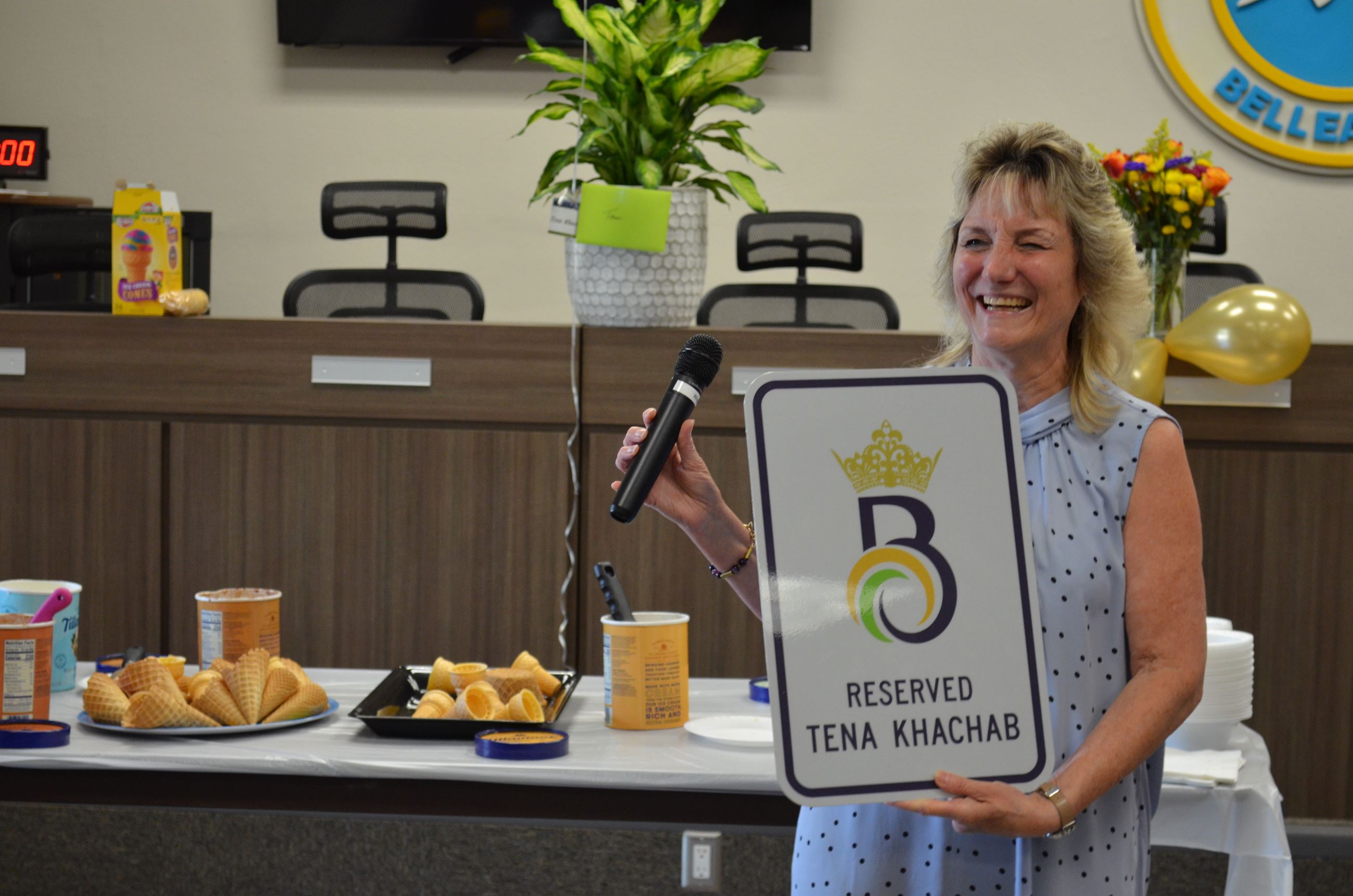 Tena smiles and laughs holding a sign that has a crown over a B and reads 