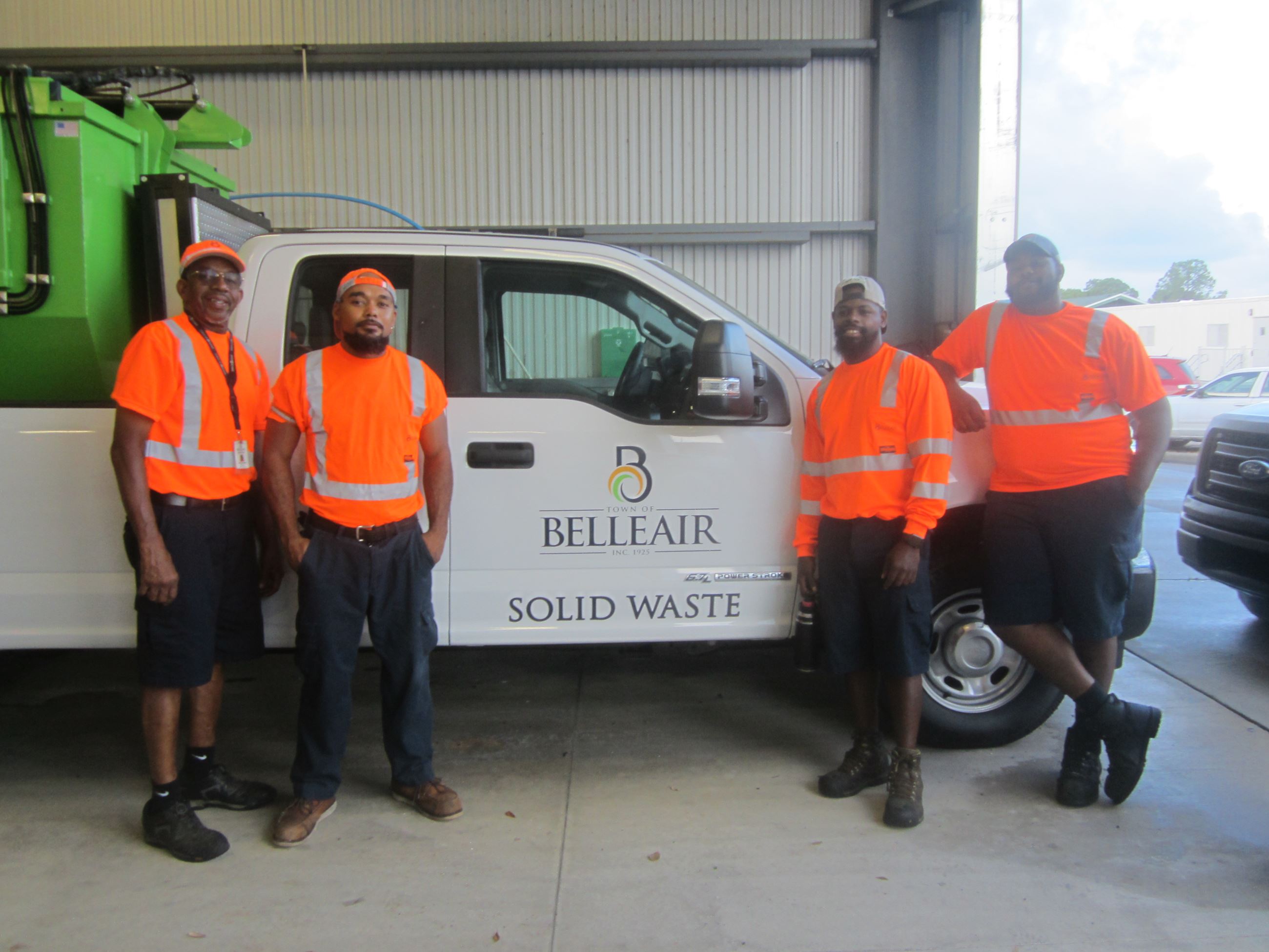 Four members of Belleair's Solid Waste Department smile in front of the Town's satellite picku