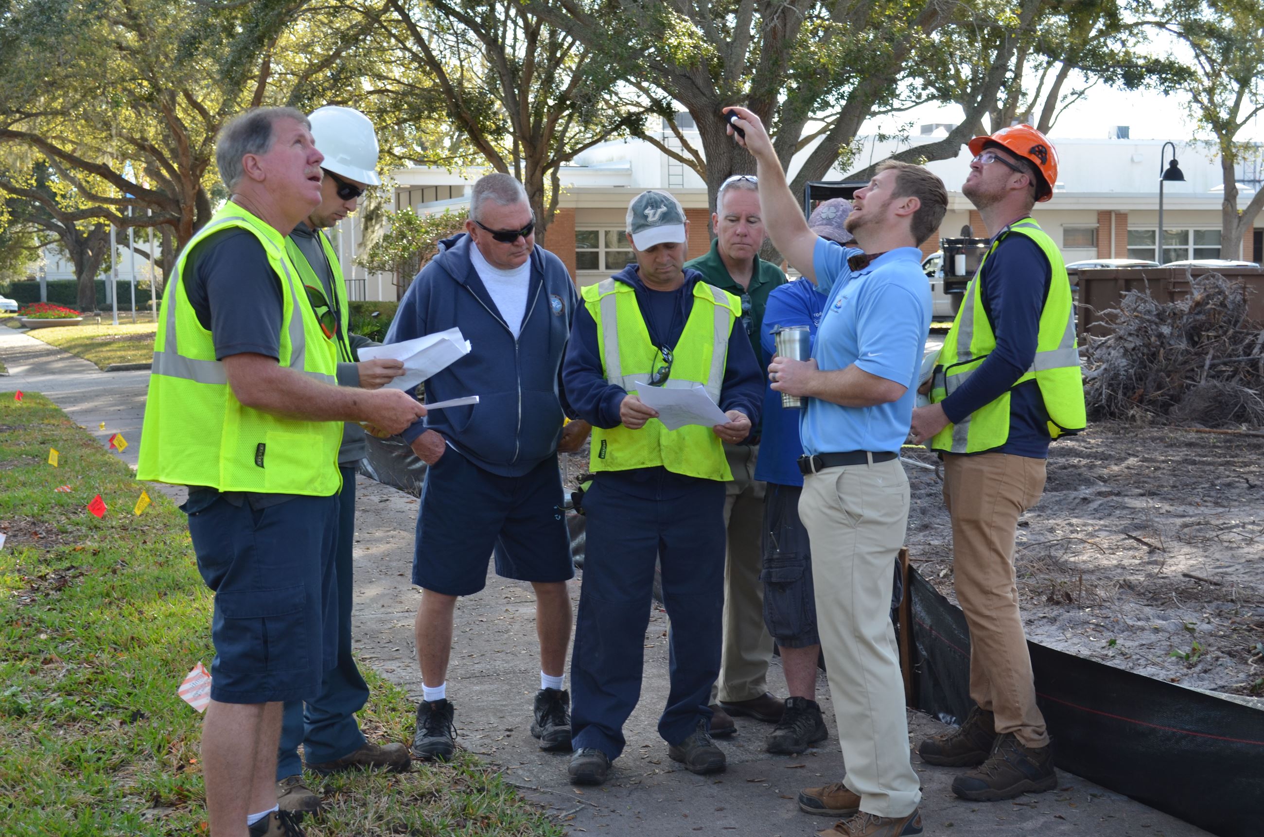 Seven members of Belleair's public works team listen to their director as he points at trees need