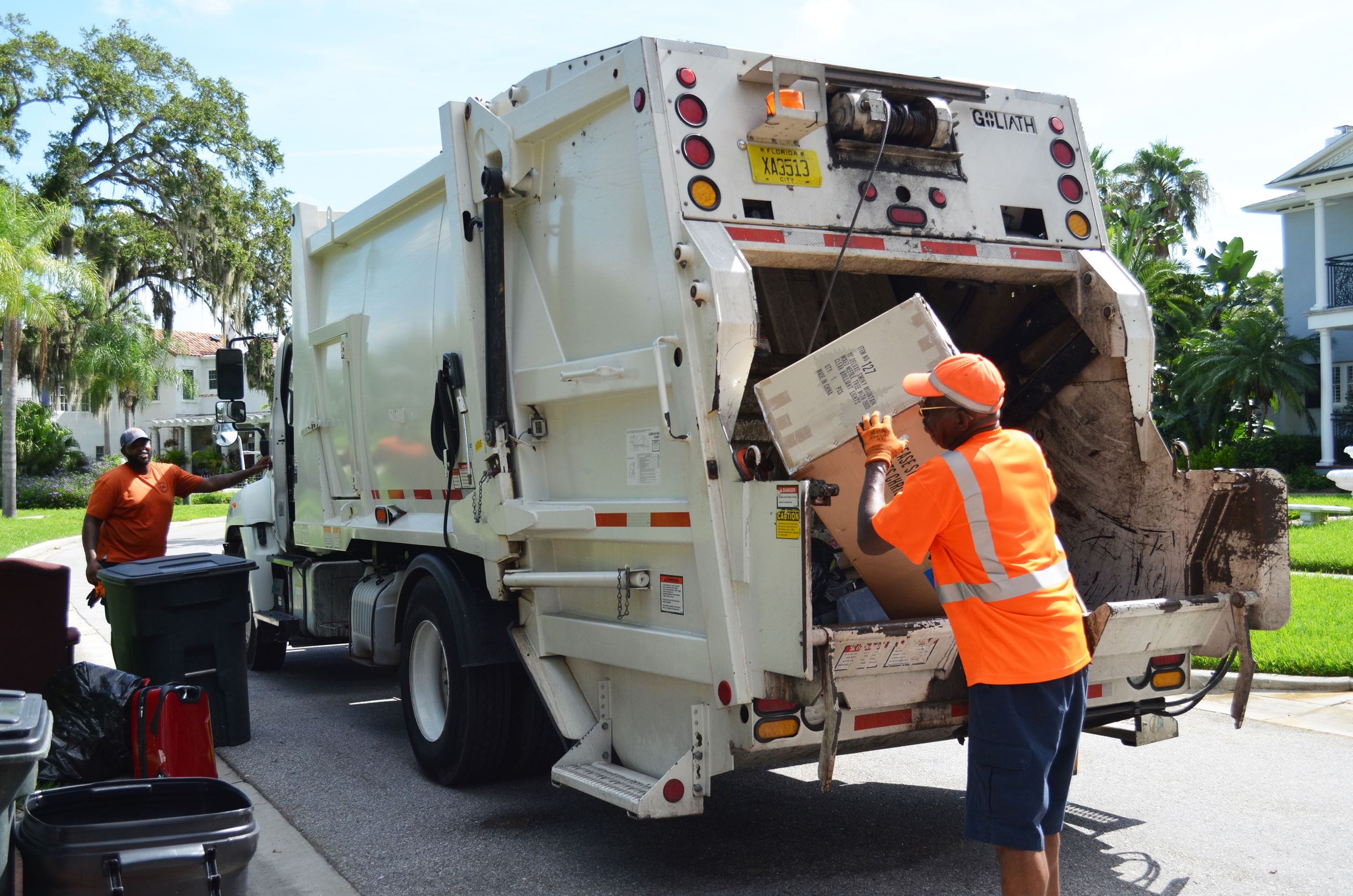 A solid waste employee dumps a trash bin into the back of a garbage truck.