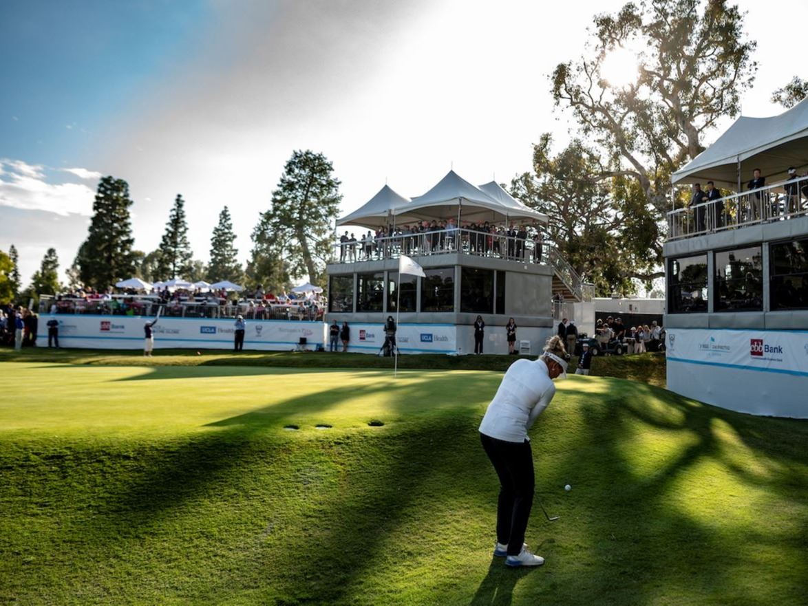 An LPGA golfer shoots her ball onto the green at a tournament match - observation stands surround he