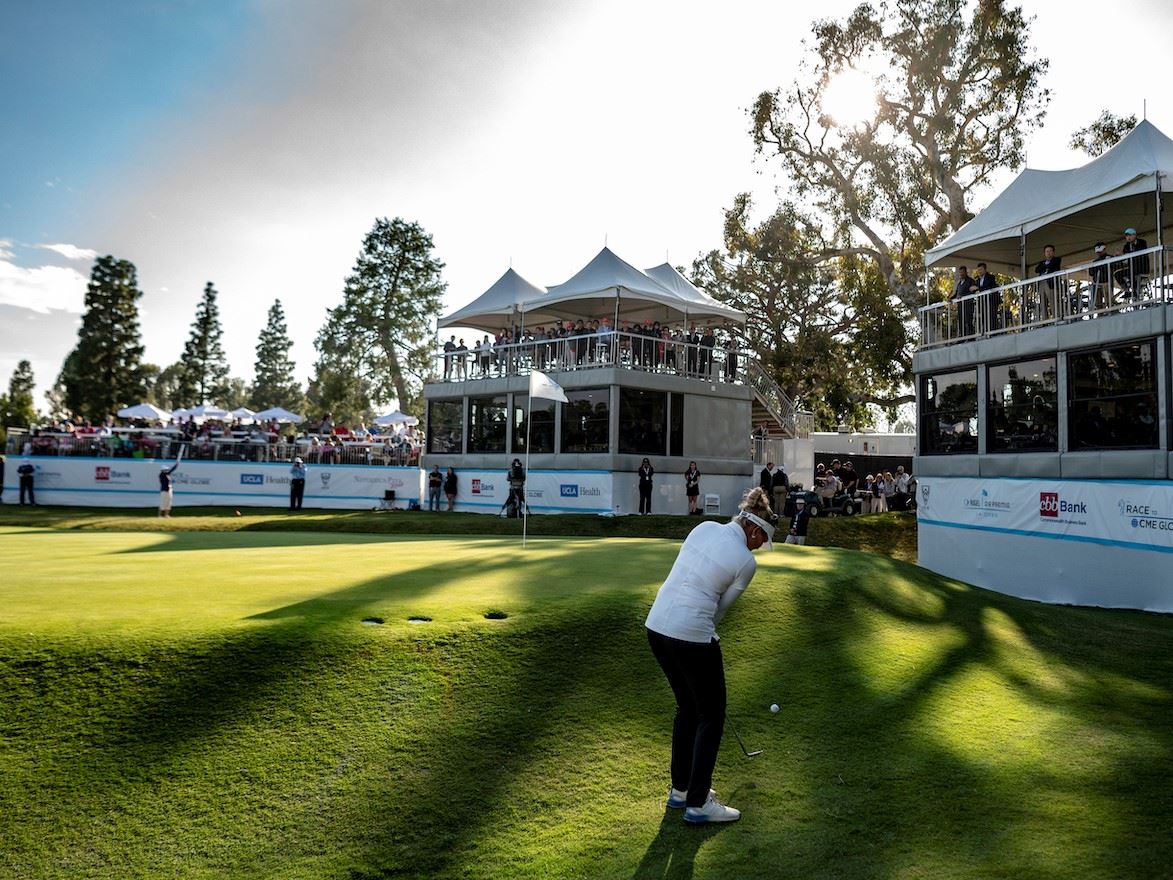 An LPGA golfer shoots her ball onto the green at a tournament match - observation stands surround he