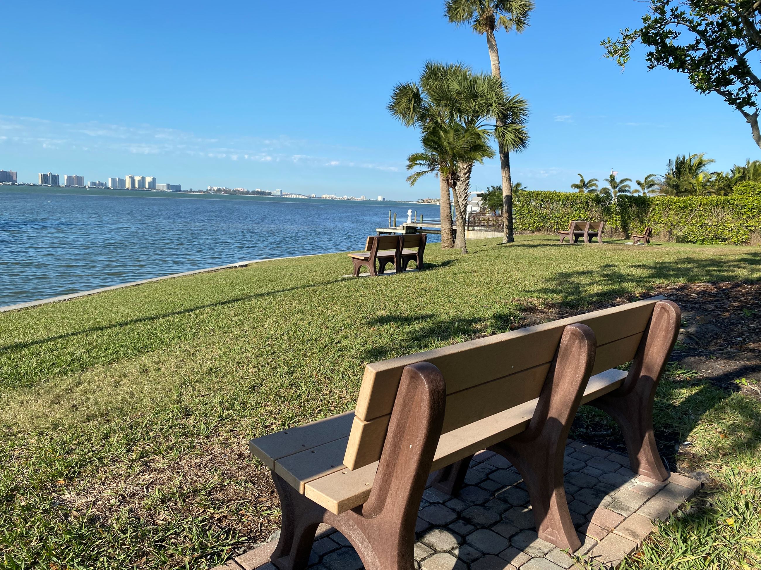 A view of the ocean is seen beyond two benches in a grassy patch at Thompson Park