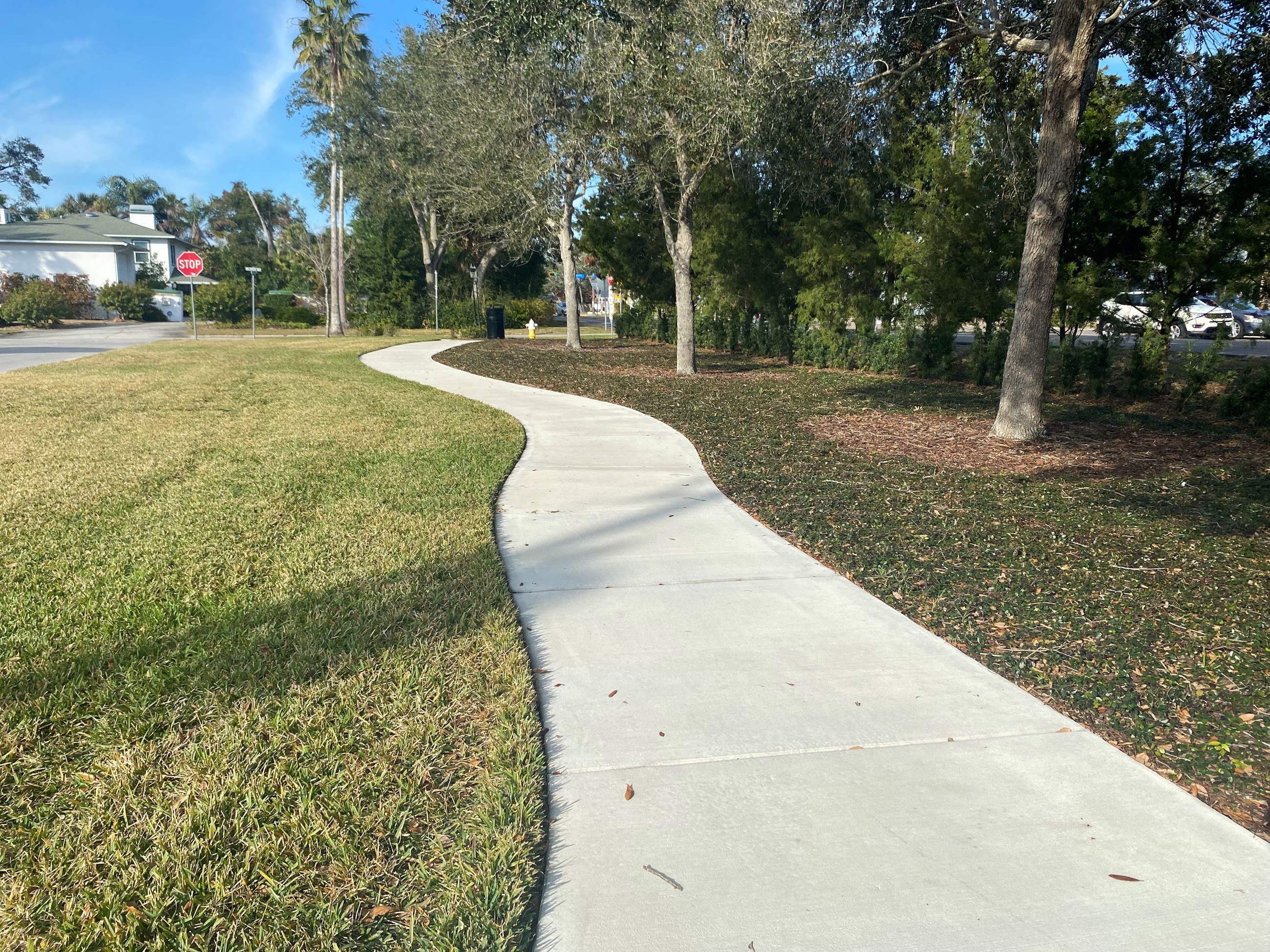 A sidewalk between two grassy patches leads to two black benches in Wildwood Park